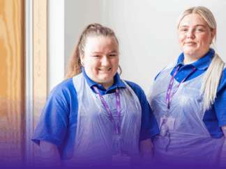 Two Care Assistant women smiling with aprons on.
