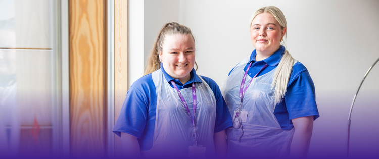 Two Care Assistant women smiling with aprons on.